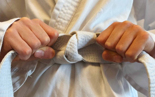 Close-up of a person tying the belt of a white martial arts uniform