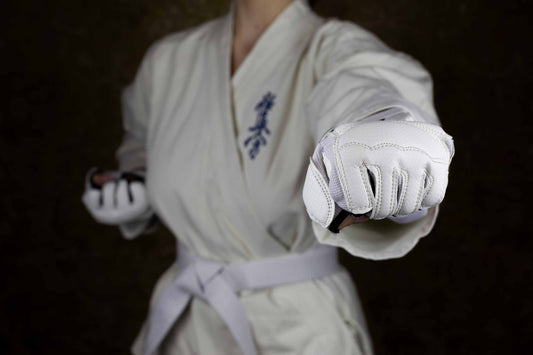 A person wearing a white martial arts uniform with a white belt and white padded gloves is shown in a fighting stance, with one fist extended forward and the other fist pulled back. The uniform has blue Japanese characters on the chest.
