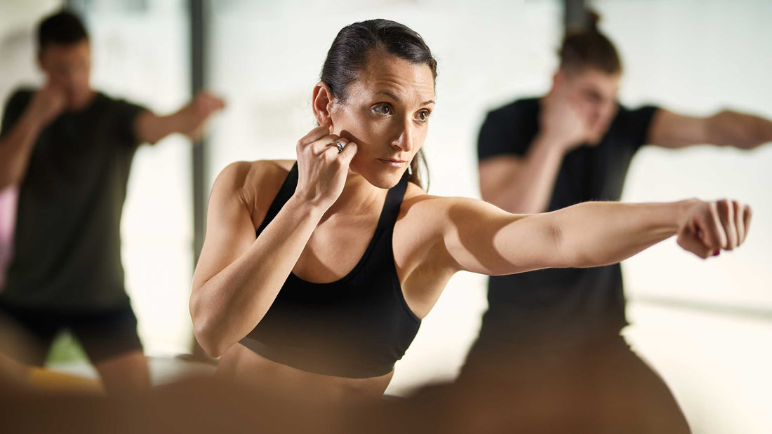 Focused woman practicing martial arts punching technique in a group hybrid cross-discipline training class.