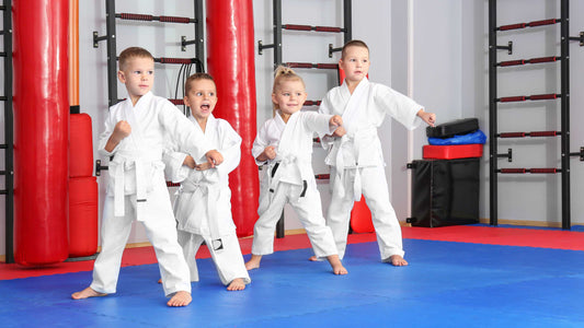 Group of young children practicing martial arts in white uniforms, performing punches on a training mat.