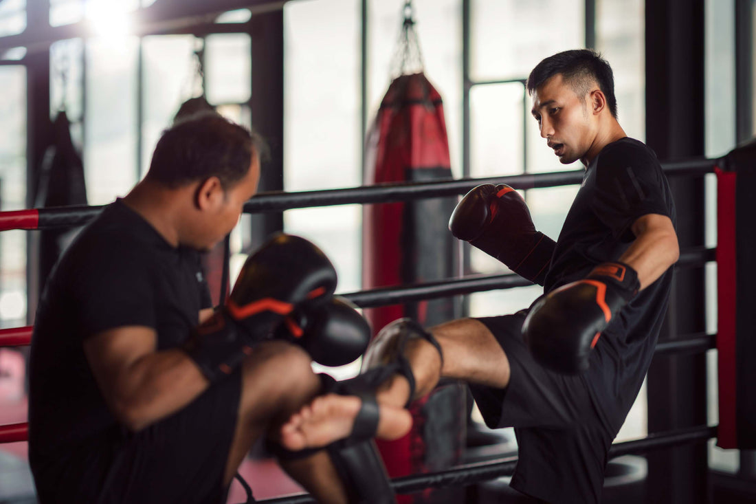 Two people practicing kickboxing in a gym, one delivering a powerful kick while the other blocks with padded gloves