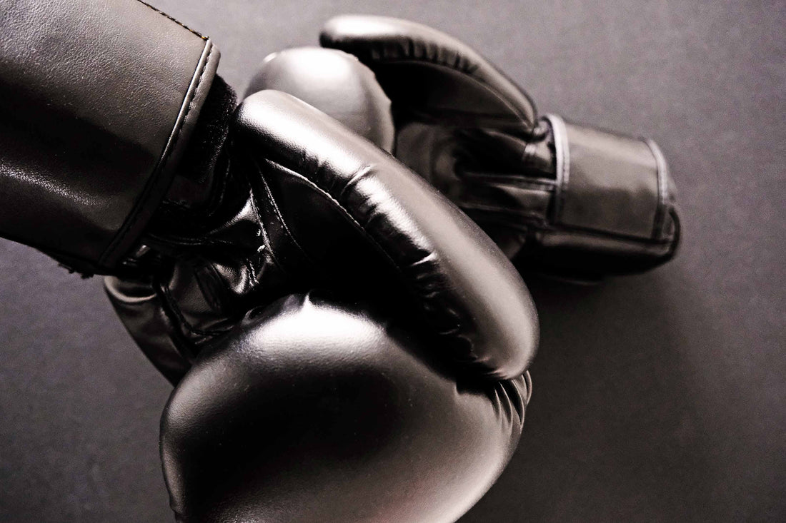 Close-up of two black boxing gloves touching each other against a dark background.